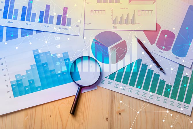 Overhead view of printed out charts and graphs set on a wood tabletop and magnifying glass on top.